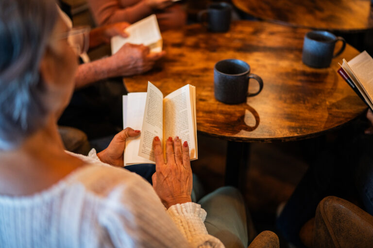 Senior woman reading a book with friends at coffee shop