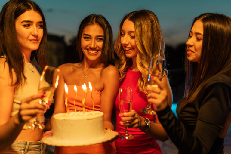 Group of young female friends celebrating birthday outdoors in city together.