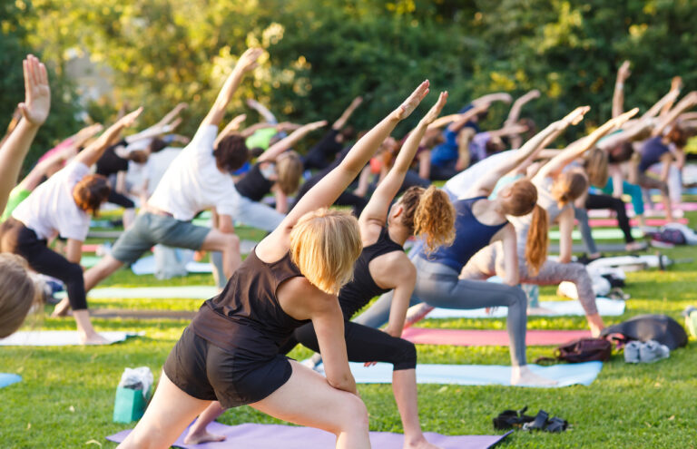 Big group of adults attending a yoga class outside.