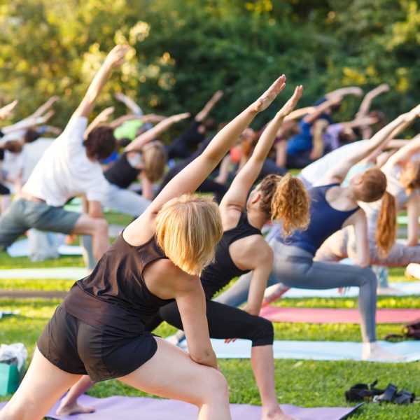 Big group of adults attending a yoga class outside.