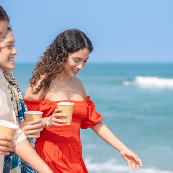 Three friends laughing and drinking coffee on the beach.